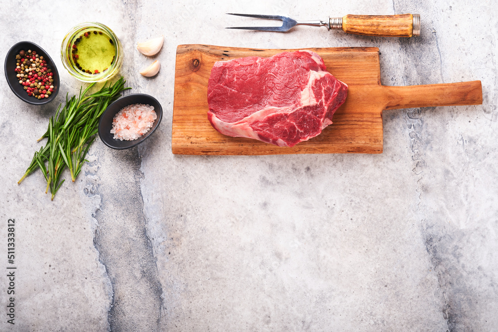 Wall mural beef steak. fresh raw beef rib eye steak with fork rosemary, salt and pepper on old wooden stand on 