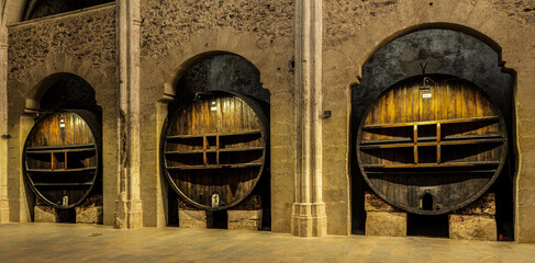 Three large old wine barrels used for aging wine on display in a stone cellar