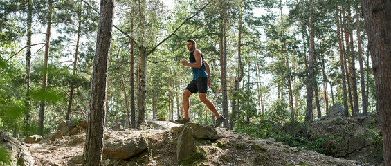 Side view of young sportsman run on hill in forest