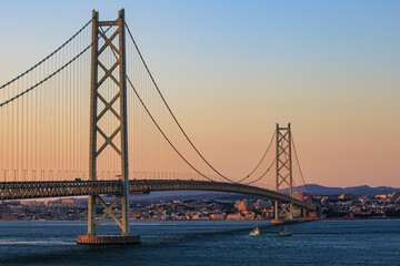 Small cargo ship passes under suspension bridge at sunset