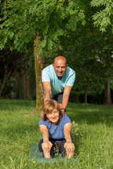 Fototapeta na wymiar Front vertical view of old couple practising yoga in the park while looking to the camera smiling and happy
