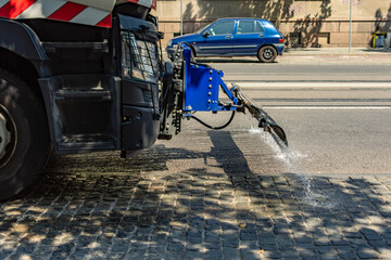 Street cleaning vehicle sprinkling or splashing water or disinfectant on asphalt on hot arid day