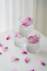 crystal glasses with tonic and floral petals on white tabletop and grey background.