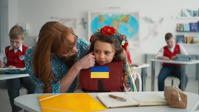 Teacher with Ukrainian schoolgirl in classroom, concept of enrolling Ukrainian kids to schools.