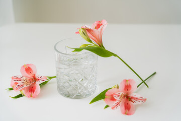 alstroemeria flowers near faceted glass with clean water on white surface and grey background.