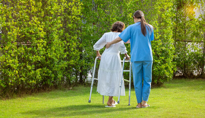  nurse takes care of an elderly woman while practicing walking with a walker in the garden at Homecare.