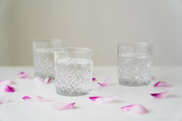 floral petals and faceted glasses with pure water on white tabletop isolated on grey.