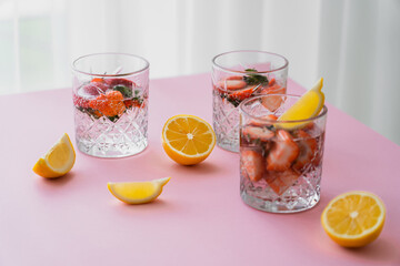 fresh tonic water with chopped strawberries near cut lemons on white tabletop.