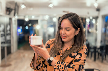 latin woman holds cream white container in her hand with copy space for advertisement, close up