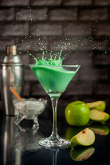 green apple smoothie juice with apple shaker and cup and glass forming a splash on black table