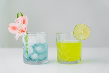 glasses of iced tonic water and lemonade with lime and tropical flower isolated on grey.