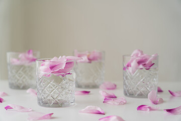 crystal glasses with tonic and petals on white surface and blurred grey background.