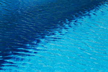 Fototapeta na wymiar Two colored light and dark blue water with ripples and sunny reflections in swimming pool.