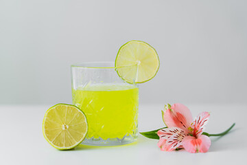 pink alstroemeria flower and sliced lime near glass of lemonade on white surface isolated on grey.