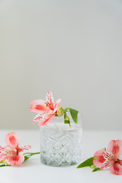 faceted glass with water near pink alstroemeria flowers on white surface isolated on grey.