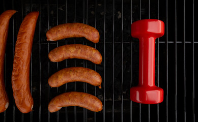 Heavy dumbbell with sausages on a grill. Fit barbecue party concept, healthy or bad diet choice,...