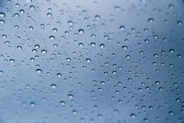 Close up of rain drops on window with blue gray background of dark sky