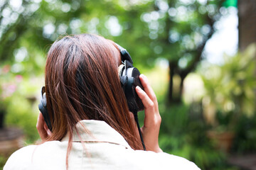 The back of an office girl who is using headphones to listen to music from a notebook with a joyful gesture in the garden.