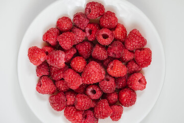 Ripe juicy raspberry on a white plate
