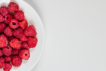 Ripe juicy raspberries on a white plate. Space for text