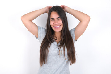 Fototapeta premium Young beautiful brunette woman wearing grey T-shirt over white wall stretching arms, relaxed position.