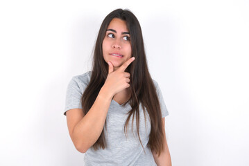Young beautiful brunette woman wearing grey T-shirt over white wall Thinking worried about a question, concerned and nervous with hand on chin.