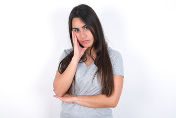 Very bored Young beautiful brunette woman wearing grey T-shirt over white wall holding hand on...