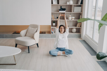 Girl is doing stretching exercises on floor at home. Happy woman is meditating with her eyes closed.