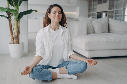 Caucasian woman is sitting in lotus asana at home in morning. Scandinavian interior of living room.