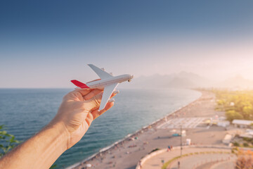 Spielzeugflugzeug in der Hand vor dem Hintergrund des berühmten Konyaalti-Strandes in Antalya - dem wichtigsten türkischen Ferienort und der Riviera. Passagierverkehr und Flüge zum Traumurlaub