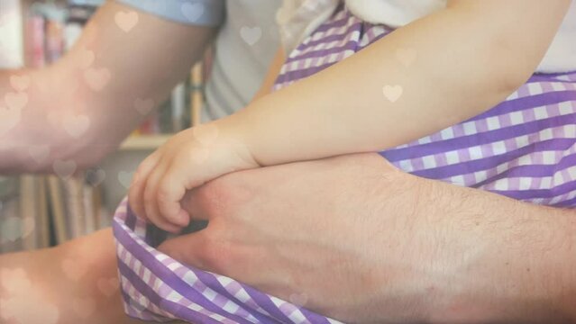 Animation of hearts floating over midsection of caucasian father and child working on laptop