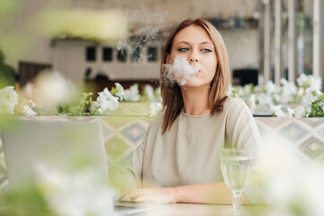 Young Woman Smoking Electronic Cigarette in the Restaurant While Working on Laptop