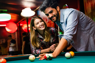 Happy young couple enjoying while playing billiard in bar. People entertainment fun concept - obrazy, fototapety, plakaty