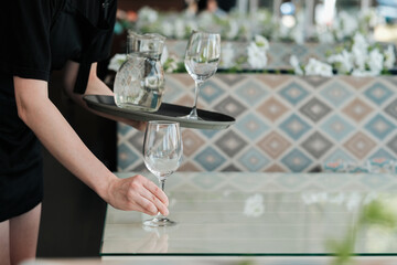 Female Waiter Serving Table with Water Glass for the Guest in Restaurant 