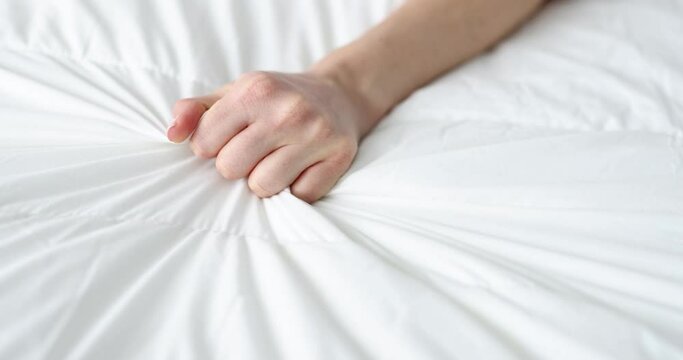 Woman's hand squeezing a white sheet on the bed