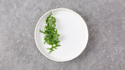 Arugula lettuce leaves on a white plate on a gray concrete background, top view