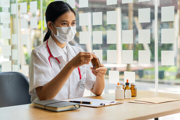 An Asian female doctor works at a hospital desk. recommend services to patients and holding a pill...