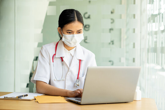 An Asian female doctor works at a hospital desk, recommending convenient online services to patients and holding a pill bottle with health care advice. disease prevention concept