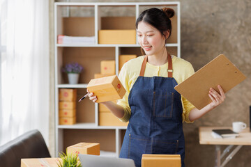 Startup SME small business entrepreneur of freelance Asian woman wearing apron using laptop and box to receive and review orders online to prepare to pack sell to customers, online sme business ideas.