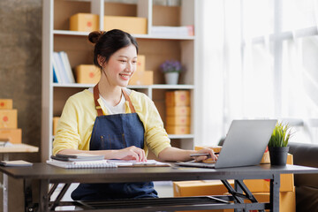 Startup SME small business entrepreneur of freelance Asian woman wearing apron using laptop and box...