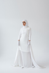 Fototapeta na wymiar full length of young muslim woman in hijab and wedding dress on grey.