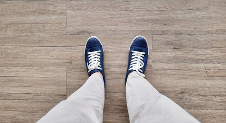 feet in denim sneakers standing on wooden vinyl floor, selective focus. fashion hipster cool man...