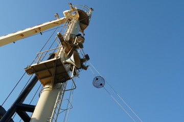 View on forward vessel mast with one black anchor ball. There are also jib of ship's crane, ladder and platform with foghorn. Behind is clear blue sky with copy space.