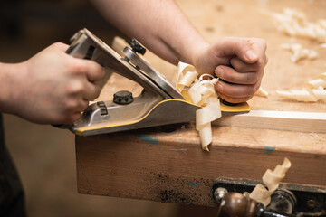 Close-up of cropped carpenter hands working with plane equipment tool on the workbench. Carpentry planer in workshop