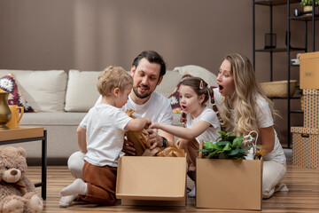 A family unpacks cardboard boxes together after moving into a new apartment. A couple and their...