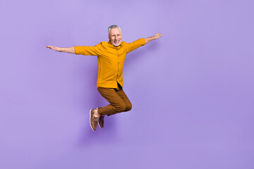 Full body photo of cheerful aged man have fun hands wings airplane isolated over purple color background