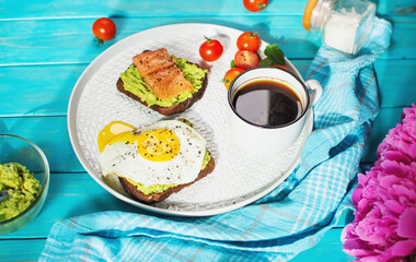 sandwich with fried egg, avocado and salted salmon with a cup of aromatic coffee for breakfast