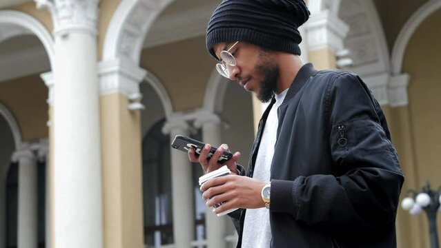 Modern Arab man stylishly dressed used mobile phone, with a cup of coffee, checks social networks and writes a message in slow motion 