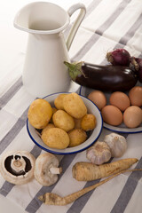 A set of essential products: milk, eggs, eggplant, garlic, potatoes, turnips and other vegetables. Rustic food on the table. White background.