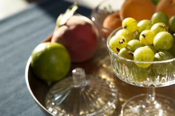 fresh berries and fruits on the table in a plate: gooseberries, currants, lemon, lime, orange, apricots. A mix of seasonal local berries and fruits lie on a vintage glass plate and a gold vintage tray